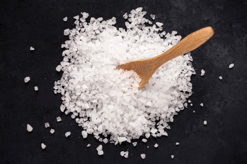 Heap of sea salt and a wooden spoon on dark background