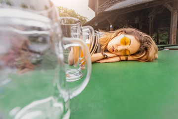 Young drunk Asian girl with hangover sleeping in Biergarten with empty beer mugs