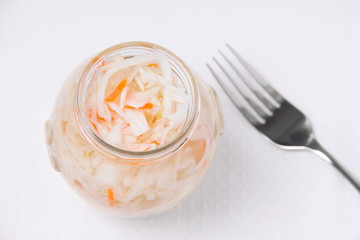 Pickled cabbage with carrots in a jar on a white background, next to a fork. Fermented vegetables