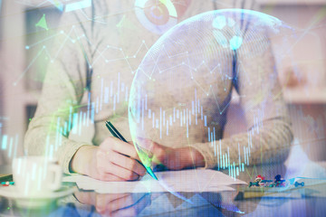 Hand taking notes in notepad. Forex chart holograms in front. Concept of research. Double exposure