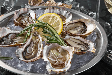 Fresh opened oysters, ice and lemon on a round metal plate, black stone textured background. Top view. Close-up shot.