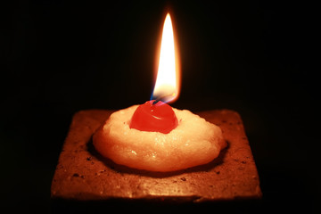 A burning cake-shaped candle with a wax cherry on top. Black background
