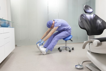 Middle age caucasian dentist stretching arms and legs .Exercises in the  office environment , during break at work