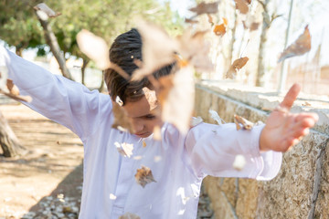 Happy arabic boy enjoying playing with dried leaves outside in th park