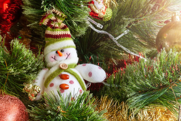 Green artificial Christmas tree decorated with beautiful smiling textile snowman, red and golden garlands, and other toys. Home decoration for a family holiday. Selective focus