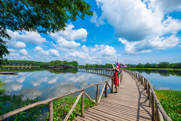 Young Asian girl walking on wood bridge cross the river and blusky with cloud  in Chumphon province.