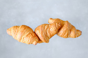 Three freshly baked croissants fly on grey background. Place for text. Creative bakery concept.