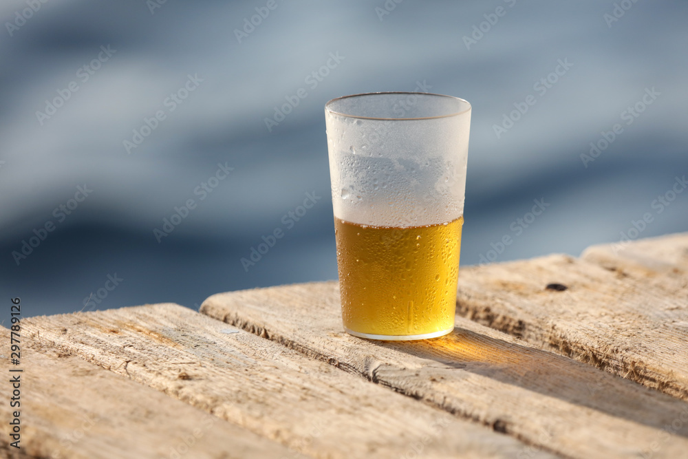 Wall mural Glass with beer near the water on the beach