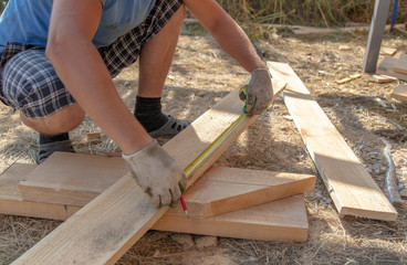 Worker measures a wooden board at a construction site