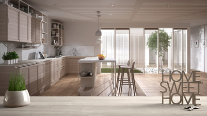 Wooden table, desk or shelf with potted grass plant, house keys and 3D letters home sweet home, over white and wooden kitchen, architecture interior design, copy space background