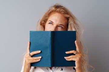 Student girl teenager holding a book in her hands over a grey background.