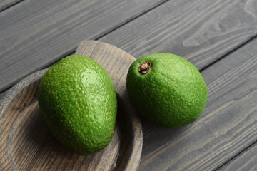 Whole fresh avocado in wooden rustic plate on dark vintage table background