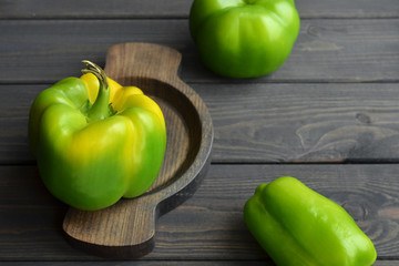 Big fresh organic green bell peppers in wooden plate on dark wooden table background, top view, copy space