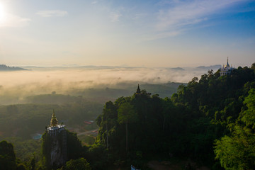 Fototapeta premium Aerial view of mountains with cloud cover mountain at sunrise, blue sky, pagoda on the mountain in Surat Thani Province, Thailand.