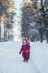Fototapeta na wymiar little cute girl 2 years old in lilac overalls walks in a winter snowy forest