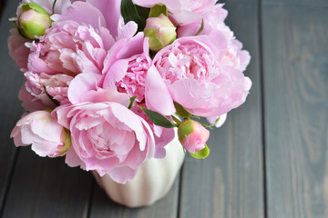Bouquet of pink peony flowers in vase on wooden background