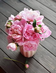Bouquet of pink peony flowers in vase on wooden background