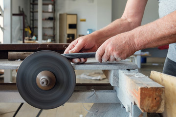 Hands of worker wich is sharpering knife on grindstone