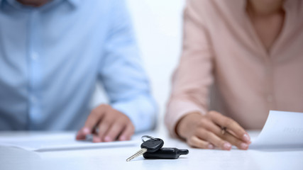 Couple signing insurance documents buying new automobile, car keys closeup