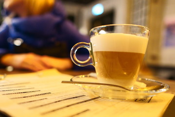 Glass mug with coffee latte in coffee on a vintage wooden table. Photo in dim light in warm colors on a wooden table with a menu under a coffee mug, lifestyle photo