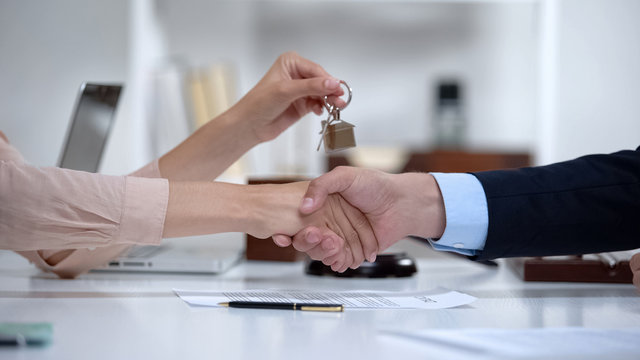 Woman shaking hands with lawyer holding house keys, successful purchase, deal
