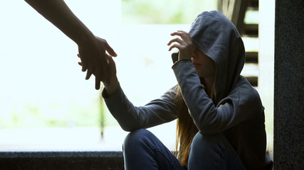 Person stretching helping hand to lonely depressed teen girl, support and aid - 297796727