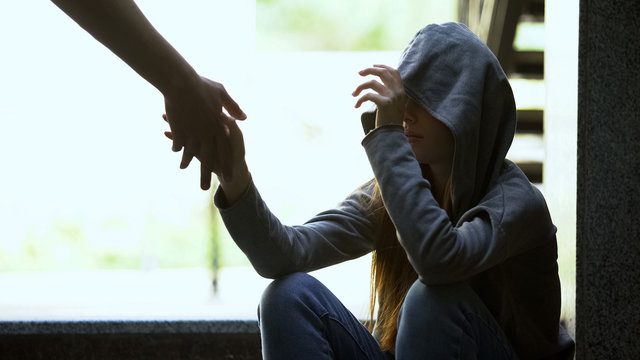 Person stretching helping hand to lonely depressed teen girl, support and aid