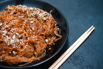 plate of Chinese cellophane rice noodles with shiitake mushrooms and peanut sauce, with sesame seeds on dark background