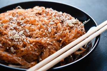 Chinese cellophane noodles with mushroom sauce of shiitake mushrooms and nuts, sesame seeds and pumpkin on a dark background,  sticks