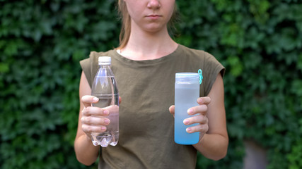 Lady choosing between reusable plastic bottle and ordinary, preventing pollution