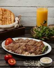 beef slices kebab on top of rice served with grilled tomato and pepper