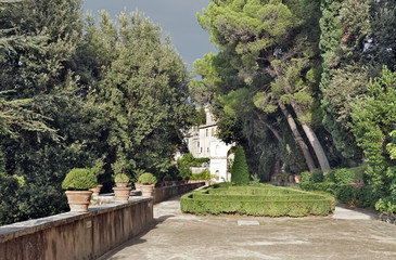 Wide walkway going between lush trees in an old Italian park with remote building