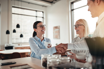 Smiling businesspeople shaking hands together during their coffe