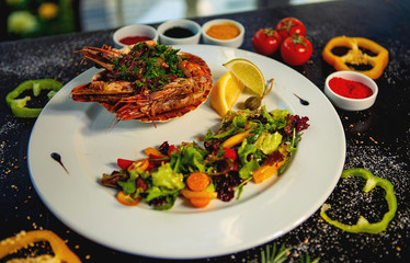 fried tiger prawn served in shell next to fresh vegetables salad and lemon