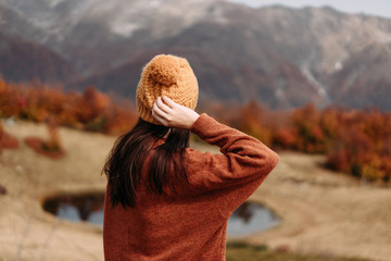 Rear view of a woman in a sweater and knitted hat on a background of mountains and a lake. Autumn...