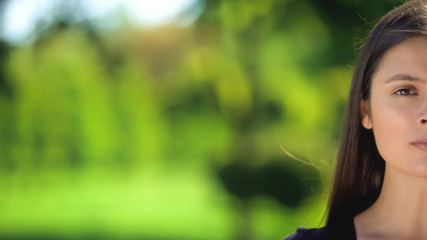 Obraz premium Half-face of young woman looking camera on blurred green background, template