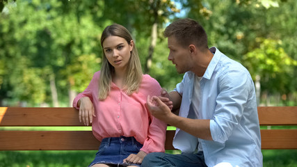 Fototapeta premium Offended woman listening to boyfriend explanations sitting park after quarrel