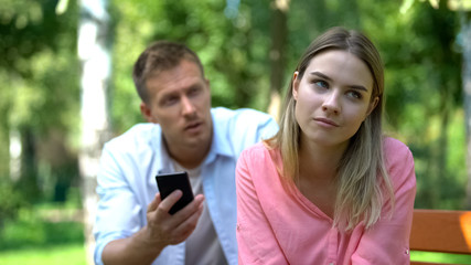 Annoyed girlfriend listening jealous boyfriend holding phone checking messages