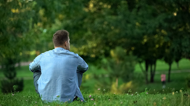 Young man sitting grass park enjoying weekend free time, loneliness, back view