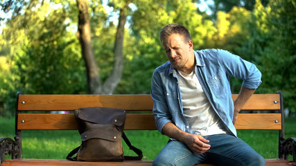Male sitting on bench suffering from lover back pain after trauma or injury