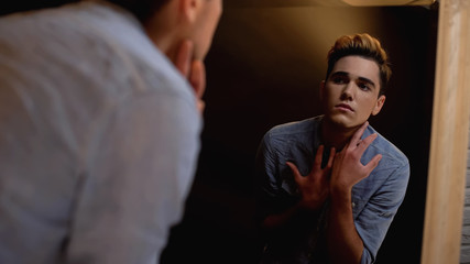 Upset gender fluid person looking in mirror and crying, self-identity problems