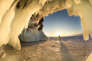 Surreal landscape with people exploring mysterious ice grotto cave. Outdoor adventure. Family exploring huge icy cave, dark majestic landscape. Magical silhouettes on background of illuminated ice