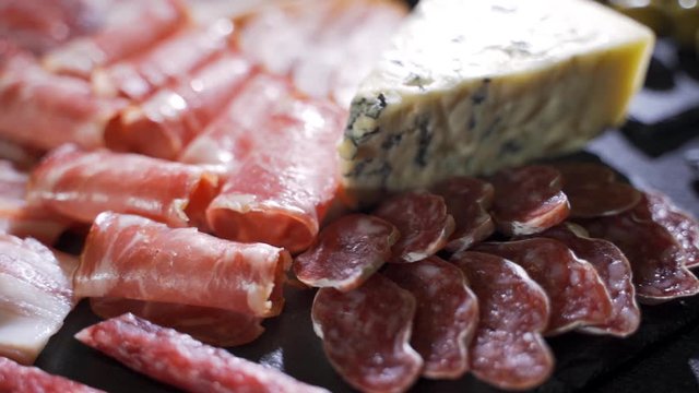 Assorted deli meats, ham, salami, bacon and tomatoes on the black stone tray