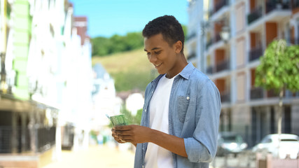 Joyful afro-american teen male counting euros, happy to go shopping, income