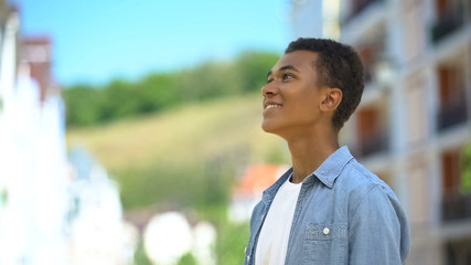 Happy mixed-race male teen inhaling pleasant bakery aroma on city street, joy