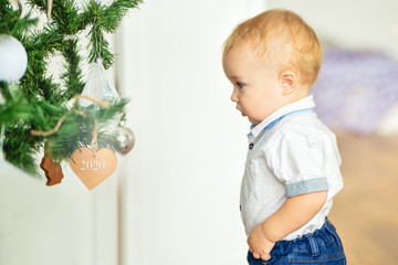 Christmas and New year. A small blond boy in a shirt and blue jeans stands next to a Christmas tree...