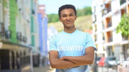 Young mixed-race male volunteer with folded arms smiling on cam outdoor, help