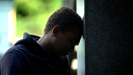 Obraz premium Depressed african american teenager sitting outdoor leaning on wall, crisis