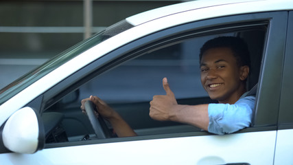 Mixed-race teenager sitting on driver seat of car showing thumbs-up, driving