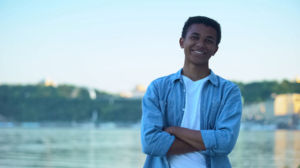 Confident multi-ethnic teenager smiling standing against river, pastime outdoor